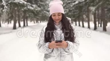 迷人的女孩穿过冬天的森林，使用智能手机。 4K